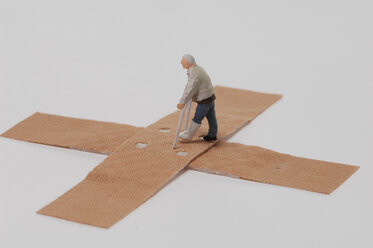 Plastic figurine walking with crutches over band-aids - ASF03726