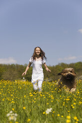 Germany, Baden Württemberg, Tübingen, Girl (12) running with dog through meadow, smiling - WESTF08940