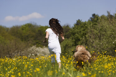 Germany, Baden Württemberg, Tübingen, Girl (12) running with dog through meadow, rear view - WESTF08939