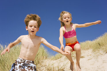 Deutschland, Ostsee, Junge (8-9) und Mädchen (6-7) springen die Stranddüne hinunter - WESTF09279