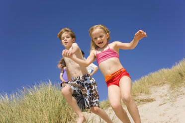 Germany, Baltic sea, Boy (8-9) and girl (6-7) jumping down beach dune - WESTF09277