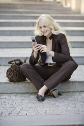 Young woman using mobile phone, sitting on steps, portrait - MAEF01053