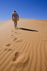 Africa, Namibia, Namib desert, Man walking over sand dune, rear view - FOF00967