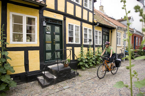 Denmark, Fuenen, Couple mountain biking alongside timbered houses stock photo