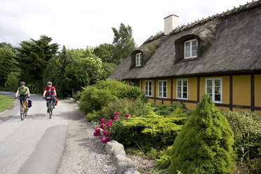 Denmark, Fuenen, Couple mountain biking alongside thatched house - DSF00181