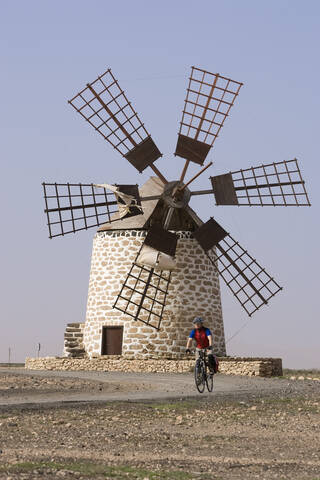 Spanien, Kanarische Inseln, Mann beim Mountainbiking, Windmühle im Hintergrund, lizenzfreies Stockfoto