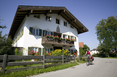 Deutschland, Bayern, Lenggries, Frau beim Mountainbiken neben Wohnhaus - DSF00132