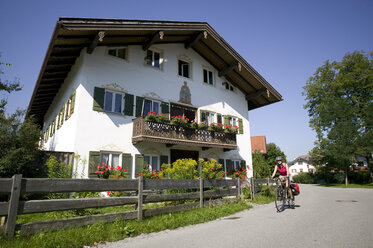 Germany, Bavaria, Lenggries, Woman mountain biking next to residential house - DSF00132