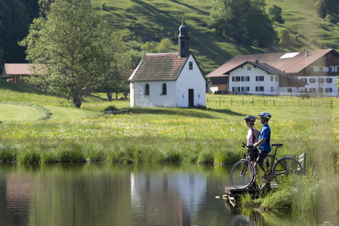 Deutschland, Bayern, Allgäu, Pärchen mit Mountainbikes am Seeufer stehend - DSF00103