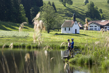 Deutschland, Bayern, Allgäu, Pärchen mit Mountainbikes am Seeufer stehend - DSF00102