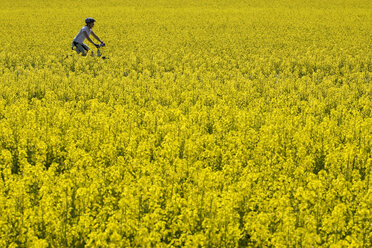 Germany, Bavaria, Oberland, Woman mountain biking across rape field - DSF00097