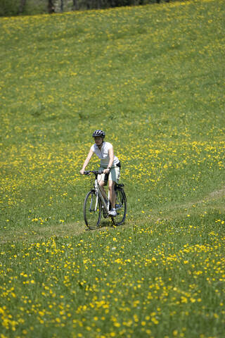 Deutschland, Bayern, Oberland, Frau fährt mit dem Mountainbike über eine blühende Wiese, lizenzfreies Stockfoto