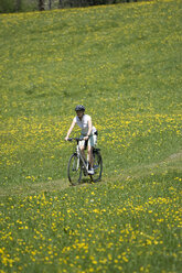 Deutschland, Bayern, Oberland, Frau fährt mit dem Mountainbike über eine blühende Wiese - DSF00095