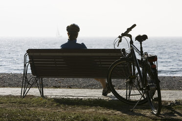 Italy, Trento, Riva del Garda, Mountaibinker taling a break, sitting on bench, rear view - DSF00089