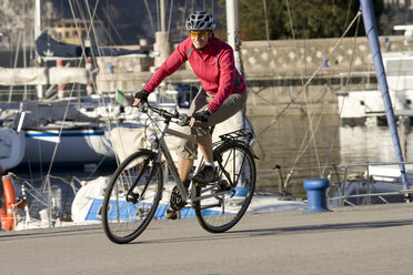 Italy, Trento, Riva del Garda, Female mountainbiker riding across pier - DSF00087