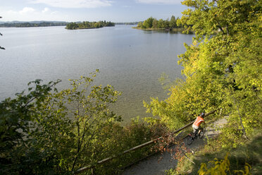 Deutschland, Bayern, Staffelsee, Person beim Mountainbiking am See entlang, Rückansicht - DSF00081