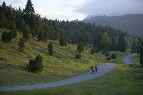 Deutschland, Bayern, Mittenwald, Pärchen beim Mountainbiken über die Landstraße, lizenzfreies Stockfoto