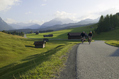 Deutschland, Bayern, Mittenwald, Pärchen beim Mountainbiken über die Landstraße - DSF00008