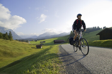 Germany, Bavaria, Mittenwald, Woman mountain biking across highway - DSF00007