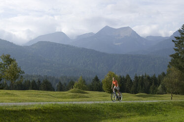 Deutschland, Bayern, Mittenwald, Frau beim Mountainbiken vor Bergkulisse - DSF00001