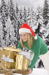 Österreich, Salzburger Land, Altenmarkt, junge Frau schiebt einen mit Weihnachtsgeschenken beladenen Schlitten - HHF02615