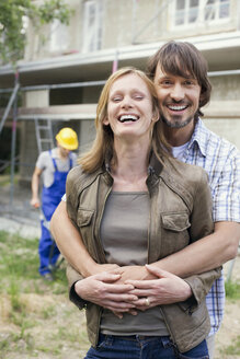Junges Paar auf der Baustelle, das sich umarmt, Bauarbeiter im Hintergrund - WESTF09154