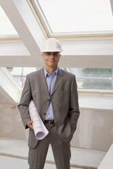 Architect at construction site holding construction plan, smiling, portrait - WESTF09120