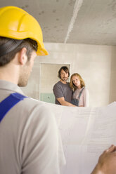 Construction worker holding construction plan, young couple in background - WESTF09084