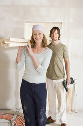 Young couple carrying wooden planks at home, portrait - WESTF09045