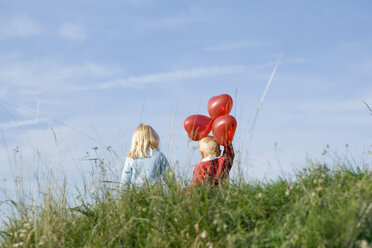 Little girl and boy (3-4) with balloons walking hand in hand, rear view - SMOF00176