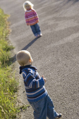 Kleines Mädchen (2-3) und Junge (1-2) spielen auf dem Weg, Rückansicht, lizenzfreies Stockfoto