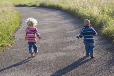 Little girl (2-3) and boy (1-2) running across path, rear view - SMOF00148