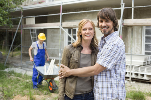 Junges Paar auf der Baustelle, das sich umarmt, Bauarbeiter im Hintergrund - WESTF09152