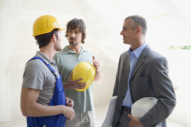 Zwei Männer im Gespräch mit einem Architekten auf einer Baustelle - WESTF08999