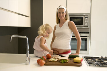 Schwangere Mutter und Tochter (3-4) in der Küche, Mutter hält schwangeren Bauch - WESTF10090