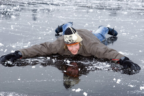 Junger Mann (16-17) in Winterkleidung auf einem zugefrorenen See liegend, lächelnd - AWDF00296