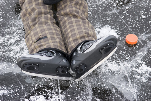 Person mit Schlittschuhen auf einem zugefrorenen See neben einem Eishockey-Puck liegend, Blick von oben - AWDF00294