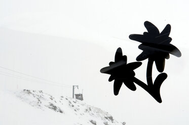 Schweiz, Arosa, Blumenförmiges Etikett auf Glasscheibe, Skilift im Hintergrund - AWDF00105