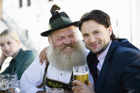 Deutschland, Bayern, Oberbayern, Mann in Tracht und Geschäftsmann im Biergarten, lächelnd, Portrait, lizenzfreies Stockfoto