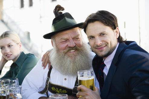 Germany, Bavaria, Upper Bavaria, Man in traditional cosume and businessman in beer garden, smiling, portrait - WESTF09723