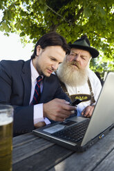Deutschland, Bayern, Oberbayern, älterer bayerischer Mann und junger Geschäftsmann mit Laptop im Biergarten - WESTF09703