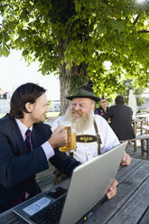 Deutschland, Bayern, Oberbayern, älterer bayerischer Mann und junger Geschäftsmann mit Laptop im Biergarten - WESTF09699