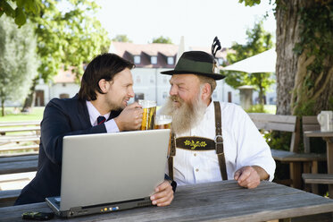 Deutschland, Bayern, Oberbayern, älterer bayerischer Mann und junger Geschäftsmann mit Laptop im Biergarten - WESTF09698