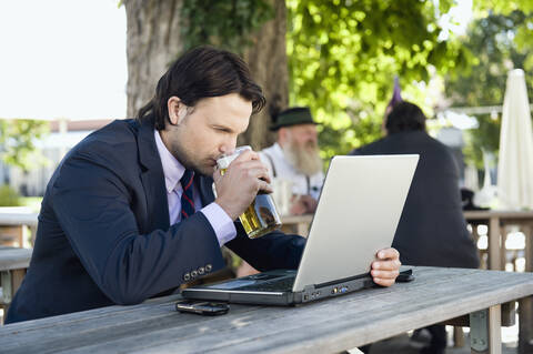 Deutschland, Bayern, Oberbayern, Junger Geschäftsmann im Biergarten beim Biertrinken, lizenzfreies Stockfoto