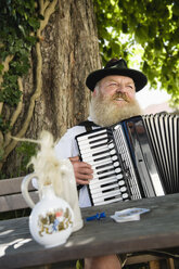 Deutschland, Bayern, Oberbayern, Älterer Mann in Tracht spielt Akkordeon im Biergarten - WESTF09660