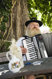 Germany, Bavaria, Upper Bavaria, Senior man in traditional costume playing accordion in beer garden - WESTF09660