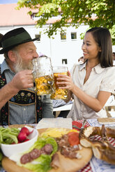 Germany, Bavaria, Upper Bavaria, Asian woman and bavarian man toasting each other - WESTF09625