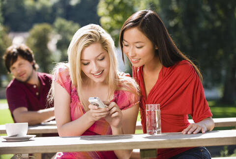 Germany, Bavaria, Upper Bavaria, Two young women in beer garden looking amused at mobile phone stock photo