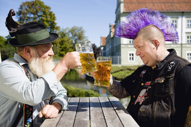 Germany, Bavaria, Upper Bavaria, Man with mohawk hairstyle and Bavarian man holding beer stein glasses - WESTF09541