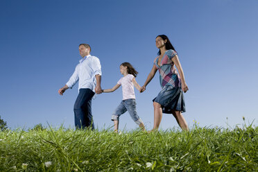 Parents and daughter (6-7) taking a walk across meadow - CLF00606
